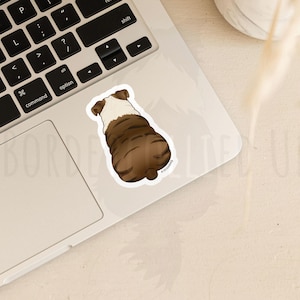 May include: A sticker featuring a brown and white bulldog from the rear. The sticker is on a laptop, with the keyboard visible. The bulldog sticker is a cartoon illustration.