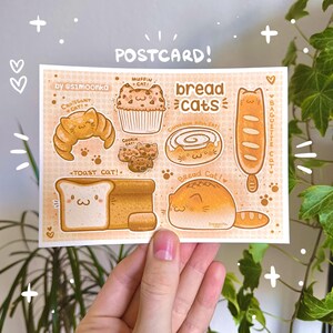 Può includere: Una cartolina con illustrazioni di gatti disegnati come prodotti da forno, tra cui un gatto croissant, un gatto muffin e un gatto toast. Il design ha uno sfondo arancione chiaro con impronte di zampe e il testo "POSTCARD!" e "bread cats."