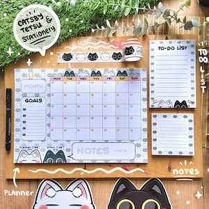 May include: A stationery set featuring a cat theme. Includes a monthly planner, to-do list pads, and decorative tape. The planner has a calendar layout with space for goals and notes. The set is decorated with cat illustrations in black and white.