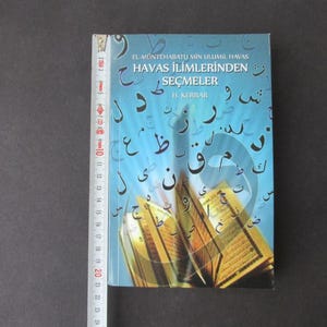 Puede incluir: Un libro azul con escritura árabe y el título "HAVAS İLİMLERİNDEN SEÇMELER" en turco. El libro trata sobre la ciencia del "havas" y está escrito por H. KERRAR.