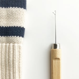 Könnte beinhalten: Eine Holznadel zum Verarbeiten von Garn mit einem Metallhaken und einer schwarzen Filzspitze. Die Nadel wird verwendet, um Garn durch Strickstoff zu weben.