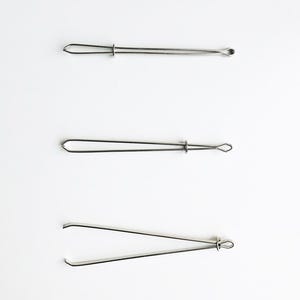 Könnte beinhalten: Drei Edelstahl-Hautpflege-Werkzeuge, jedes mit einem anderen Spitzendesign, angeordnet auf weißem Hintergrund. Das obere Werkzeug hat an einem Ende eine Schlaufe und am anderen eine spitze Spitze. Das mittlere Werkzeug hat an beiden Enden eine Schlaufe. Das untere Werkzeug hat abgewinkelte Spitzen.