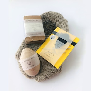 Może przedstawiać: Zestaw narzędzi do cerowania, w tym drewniane jajko do cerowania, opakowanie przędzy do cerowania oraz zestaw igieł i nawlekacza. Jajko do cerowania jest z jasnego drewna. Opakowanie przędzy jest oznaczone "DARNING YARN" i "STOPFGARN". Zestaw igieł znajduje się w żółtym opakowaniu.