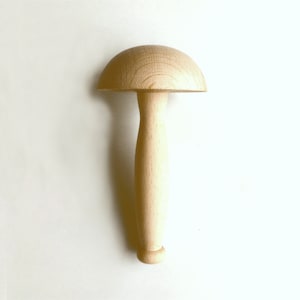 Może przedstawiać: Drewniane narzędzie w kształcie grzyba z zaokrąglonym wierzchołkiem i długim, smukłym uchwytem. Narzędzie wykonane jest z jasnego drewna i wydaje się nowe. Uchwyt jest gładki i cylindryczny, a wierzchołek to półkula. Narzędzie jest prawdopodobnie używane do kształtowania lub wygładzania.