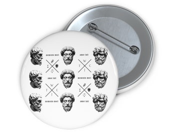 May include: A white button with a black and white design featuring nine images of the same bust of a man with different text surrounding each image. The text includes "memento mori", "amor fati", "W", "T", "J", "C", and "※".