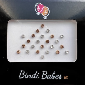 May include: A black box containing a collection of small, round, adhesive rhinestones in silver and gold tones. The text "Bindi Babes uk" is printed in white on the box.