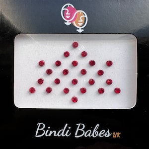 May include: A sheet of red jewel-toned adhesive bindis arranged in a diamond shape. The bindis are on a white background with the text "Bindi Babes UK" at the bottom.