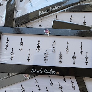 May include: A black rectangular box with a clear window displaying several black temporary tattoo designs. The designs are various shapes and sizes, including floral and geometric patterns. The text "Bindi Babes uk" is visible on the box.