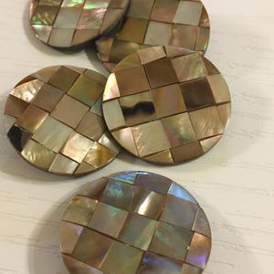 May include: Five round, iridescent, mother-of-pearl buttons with a woven pattern. The buttons are brown, gold, and green.