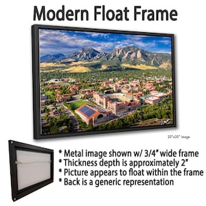 May include: A modern float frame displaying a scenic landscape of a city nestled at the foot of mountains under a blue sky. The frame is black, with a 3/4" wide frame and a thickness of approximately 2". The image size is 20"x30".
