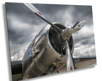 May include: A close-up of a silver airplane propeller with a cloudy sky in the background. The propeller is shiny and reflects the light. The airplane is a vintage model with a classic design.