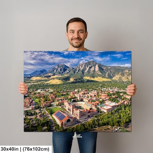 May include: A canvas print featuring an aerial view of a city nestled at the base of majestic mountains under a blue sky. The print measures 30x40 inches (76x102cm). The city has red-roofed buildings and a large stadium.