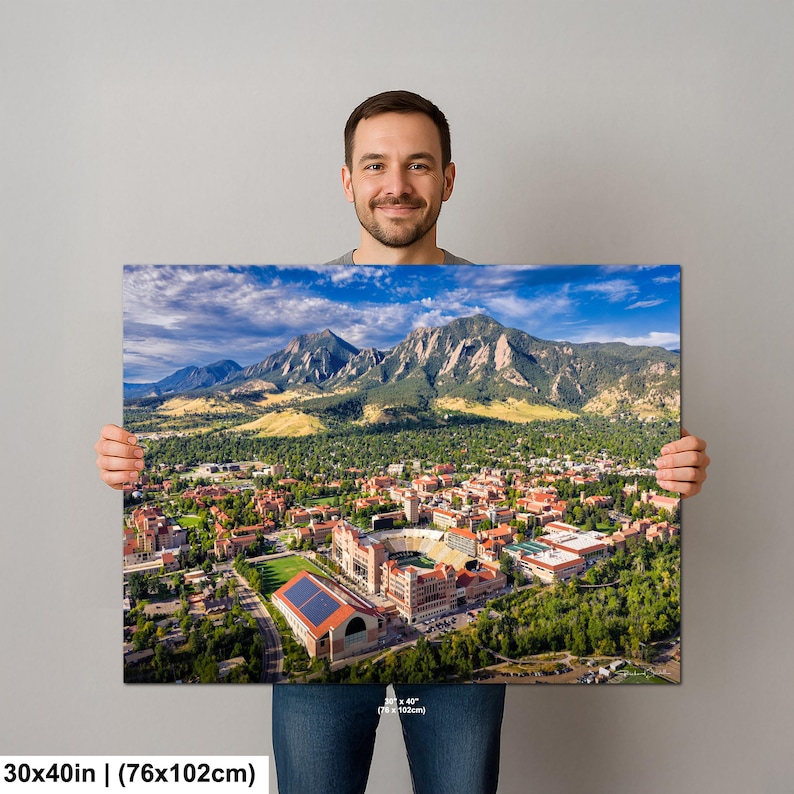 May include: A canvas print featuring an aerial view of a city nestled at the base of majestic mountains under a blue sky. The print measures 30x40 inches (76x102cm). The city has red-roofed buildings and a large stadium.