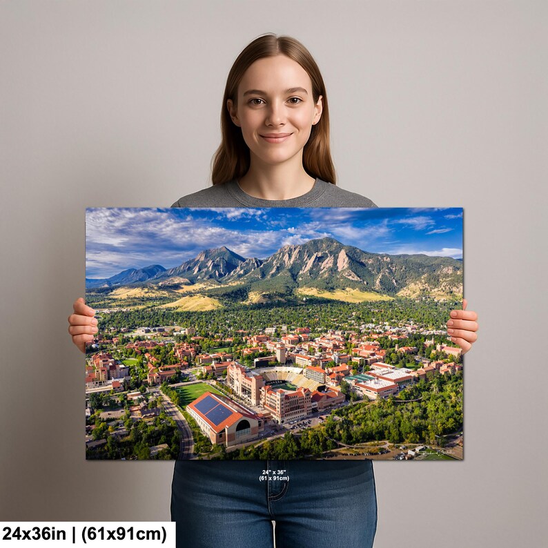 May include: A 24x36 inch (61x91cm) canvas print featuring an aerial view of a college campus nestled at the base of majestic mountains under a blue sky. The print showcases a stadium, buildings, and lush greenery.