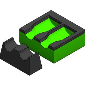 May include: A two-part object consisting of a rectangular block with a bright green interior and a black top frame featuring two recessed channels, alongside a separate black wedge-shaped piece with two curved indentations on its top surface.