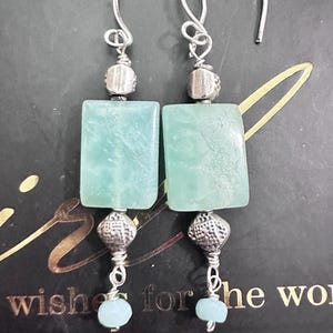 May include: A pair of silver earrings with light blue rectangular stones and smaller round stones. The earrings have a dangling design.