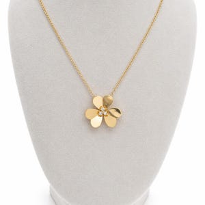 May include: A gold chain necklace featuring a three-petaled flower pendant. The pendant is crafted from polished gold and is accented with three small, clear, round-cut stones set in the center of the flower petals, creating a bright, reflective finish.