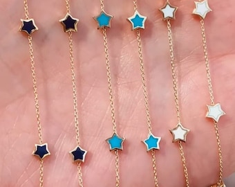 May include: Five gold chains with star-shaped charms. The stars are in different colors: black, turquoise, and white.