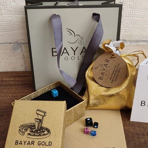 May include: A gold gift bag with a white ribbon and a brown tag that says "BAYAR GOLD" and "Bizi Trendyol'da değerlendirdiğiniz i&ccedil;in teşekk&uuml;r ederiz."  The bag is sitting on a brown surface with a gold box and a small gold pouch with a brown tag that says "BAYAR GOLD".