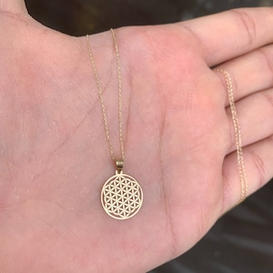 May include: A gold chain necklace with a round pendant featuring a detailed flower of life design.