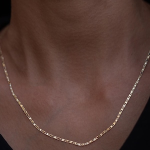 May include: A gold chain necklace with a delicate, mariner link design. The chain is worn on a person's neck.