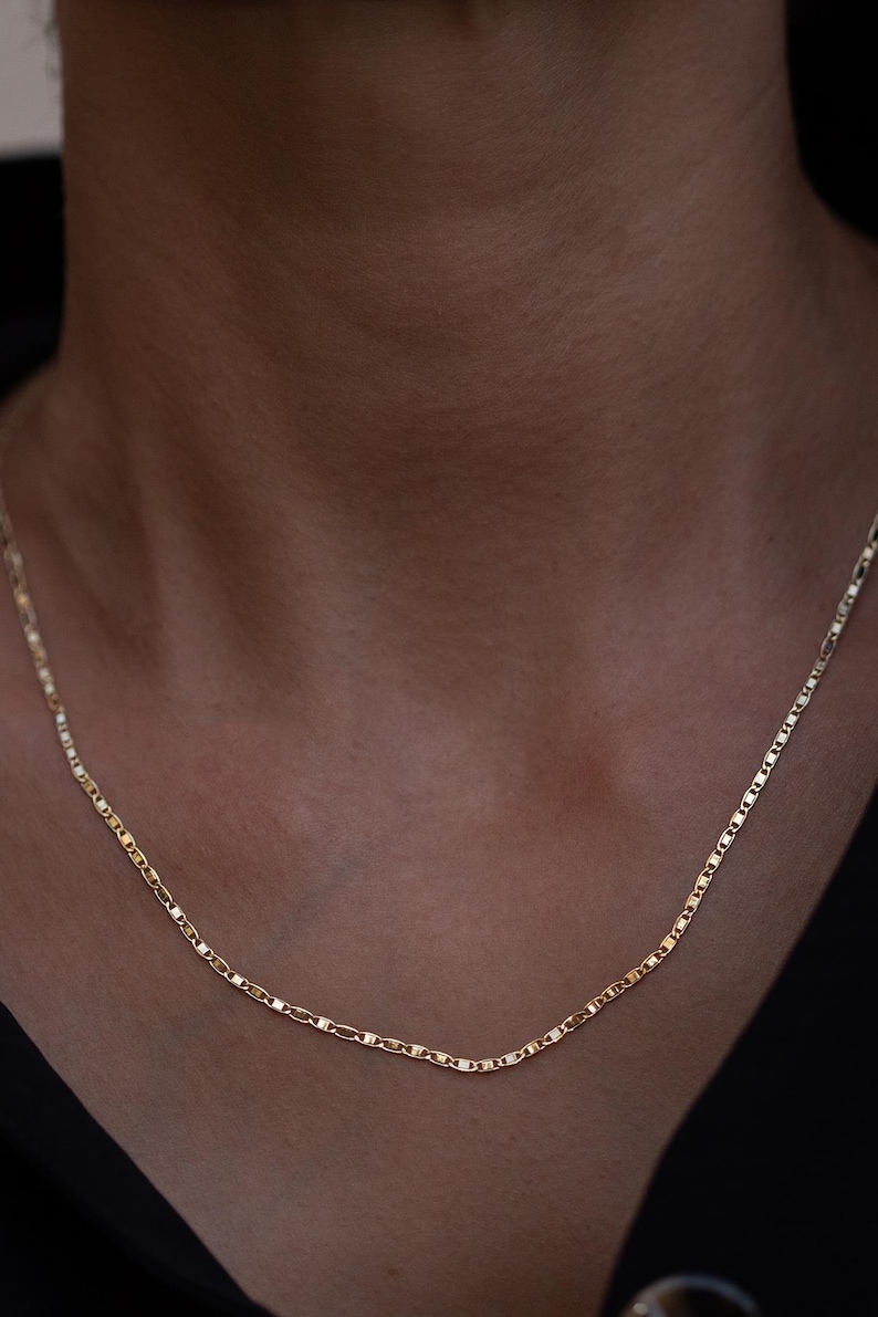 May include: A gold chain necklace with a delicate, mariner link design. The chain is worn on a person's neck.