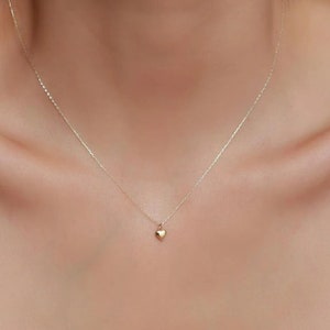 May include: A delicate gold chain necklace with a small, heart-shaped pendant.