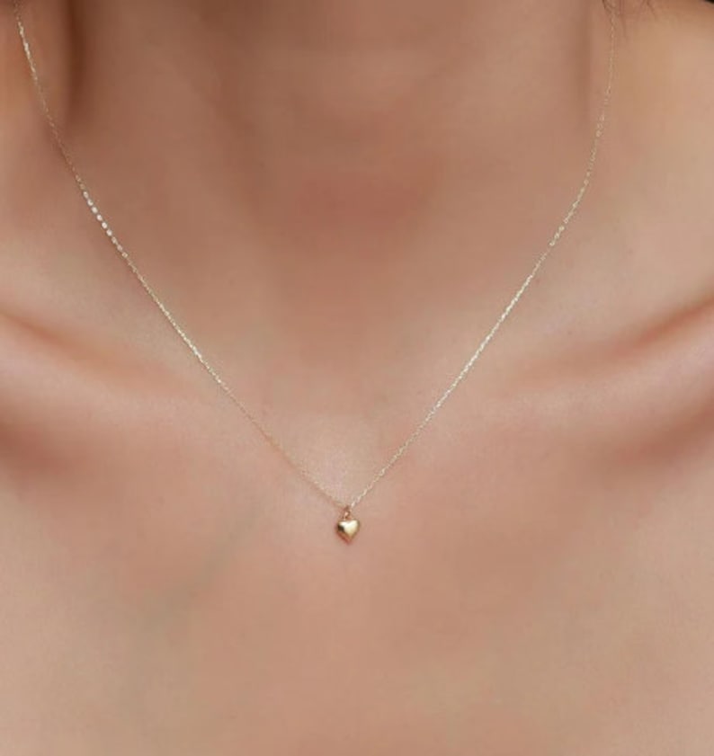 May include: A delicate gold chain necklace with a small, heart-shaped pendant.