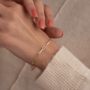 Könnte beinhalten: Ein goldenes Kettenarmband mit einem einfachen, verlinkten Design. Das Armband wird am Handgelenk getragen.