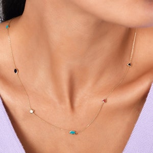 Puede incluir: Un collar de cadena de oro con una variedad de pequeños colgantes, incluyendo una estrella, un corazón, un triángulo, un óvalo y un elefante. Los colgantes son de diferentes colores, incluyendo azul, rojo y negro.