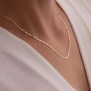 May include: A delicate gold chain necklace with a simple, elegant design. The chain is made of small, linked oval shapes.