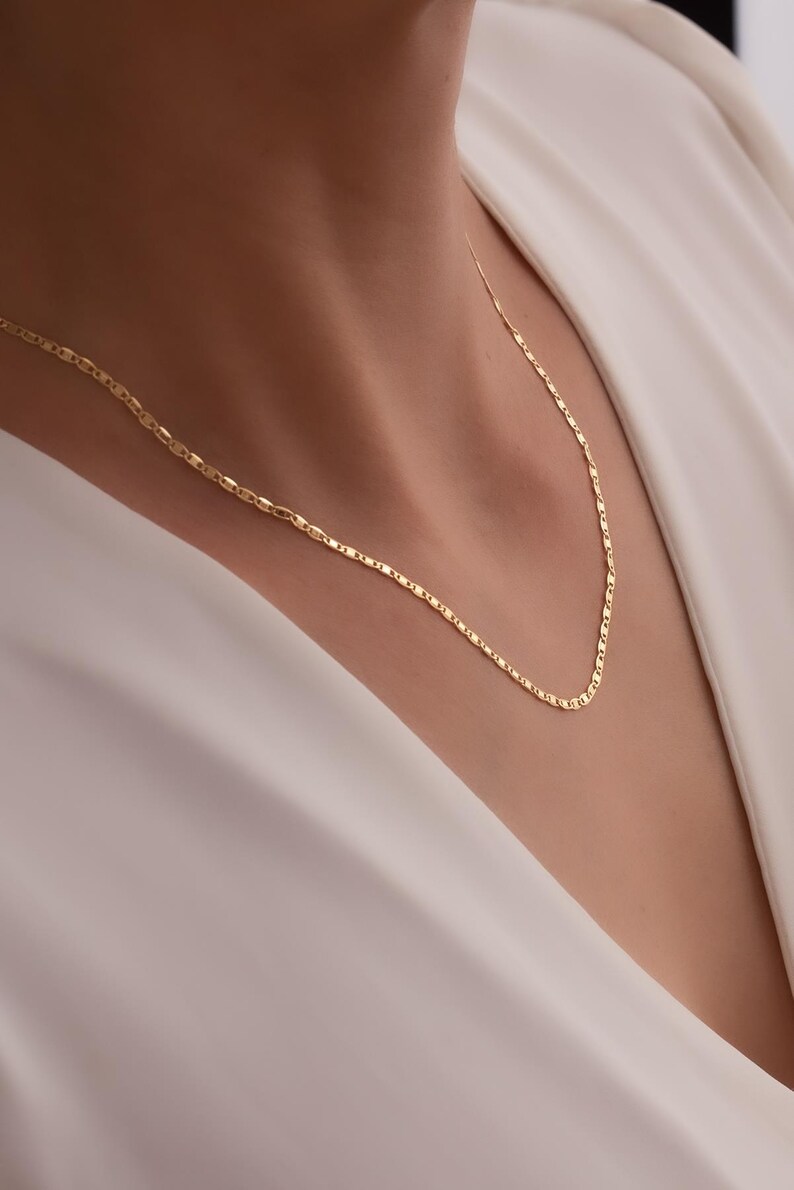 May include: A delicate gold chain necklace with a simple, elegant design. The chain is made of small, linked oval shapes.