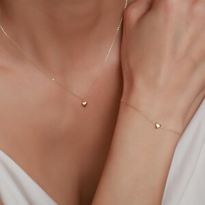 May include: A gold necklace and bracelet with a small heart pendant on each piece.
