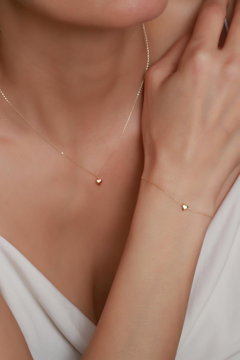 May include: A gold necklace and bracelet with a small heart pendant on each piece.