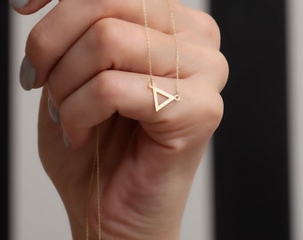 May include: A gold chain necklace with a delicate triangle pendant. The pendant is hollow and has a simple, geometric design.