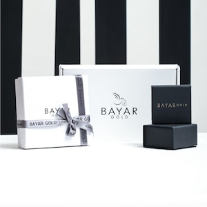 May include: Two white gift boxes with a silver ribbon and the text "BAYAR GOLD" on them. A smaller black box with the text "BAYAR GOLD" is in front of the boxes.