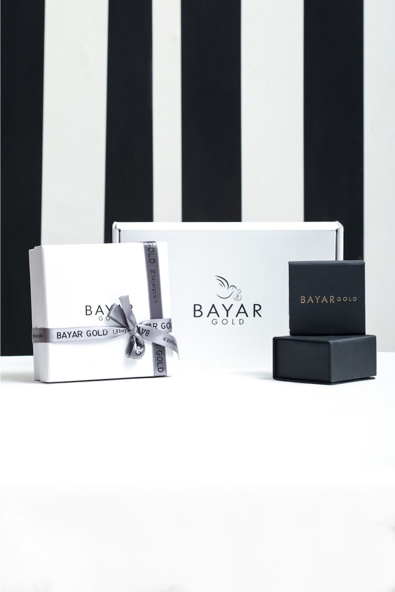 May include: Two white gift boxes with a silver ribbon and the text "BAYAR GOLD" on them. A smaller black box with the text "BAYAR GOLD" is in front of the boxes.