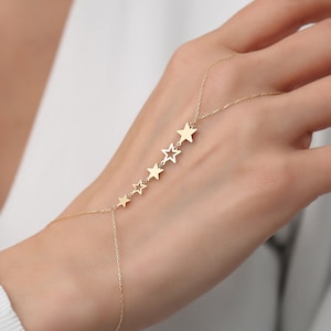 May include: A gold chain bracelet with five star charms. The bracelet is designed to be worn on the wrist and up the hand, with the stars dangling down the fingers.