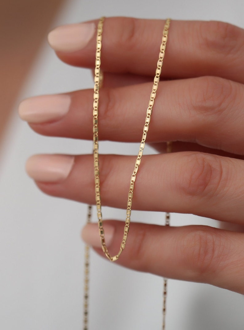 May include: A gold chain necklace with a delicate, box chain design. The chain is thin and has a subtle shine.