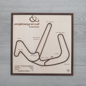 May include: A wooden map of the Anglesey Circuit race track in Wales. The map is framed in brown wood and features the track layout with turn numbers and names like "The Hairpin", "The Banking", and "Tom Price Straight". The map also includes the track's length, opening year, and number of turns.