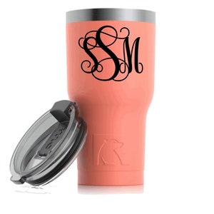 May include: A coral-colored insulated tumbler with a black monogram of the letters "SM". The tumbler has a silver rim and a clear lid. A bear logo is embossed on the side of the tumbler.