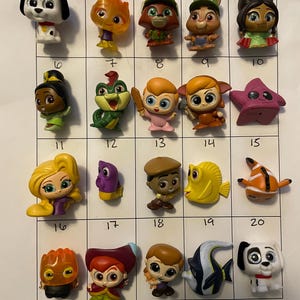 May include: A collection of twenty small, colorful figurines, each depicting a different cartoon character. The figurines are arranged in a grid pattern on a white surface. The characters include a Dalmatian, a frog, and a starfish.