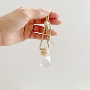 May include: A clear glass bottle with a wooden cap and a gold and white string hanging from it. The bottle is shaped like a diamond and is filled with a clear liquid.