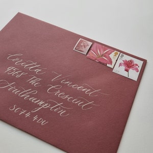 May include: A pink envelope with white calligraphy that reads "Coretta Vincent 9565 The Crescent Southampton SO74 4DU". The envelope has three stamps with floral designs.