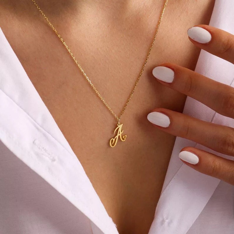 May include: A gold necklace featuring a cursive letter 'A' pendant with a small heart detail.
