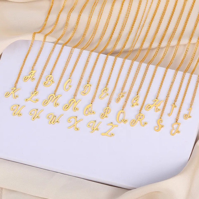 May include: A set of 26 gold-tone necklaces, each featuring a cursive letter charm. The letters range from A to Z.