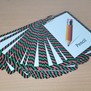 Op de afbeelding: Een set flashcards bijeengehouden door een metalen ring. Elke kaart heeft een witte achtergrond met een kleurrijke rand van afwisselende rode, zwarte en groene diagonale strepen. E&eacute;n kaart toont een potloodillustratie met het woord "Pencil".