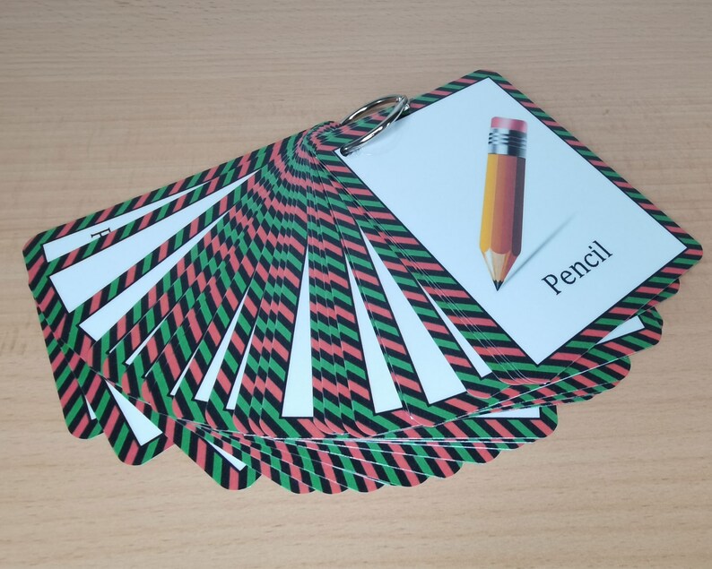 Op de afbeelding: Een set flashcards bijeengehouden door een metalen ring. Elke kaart heeft een witte achtergrond met een kleurrijke rand van afwisselende rode, zwarte en groene diagonale strepen. E&eacute;n kaart toont een potloodillustratie met het woord "Pencil".