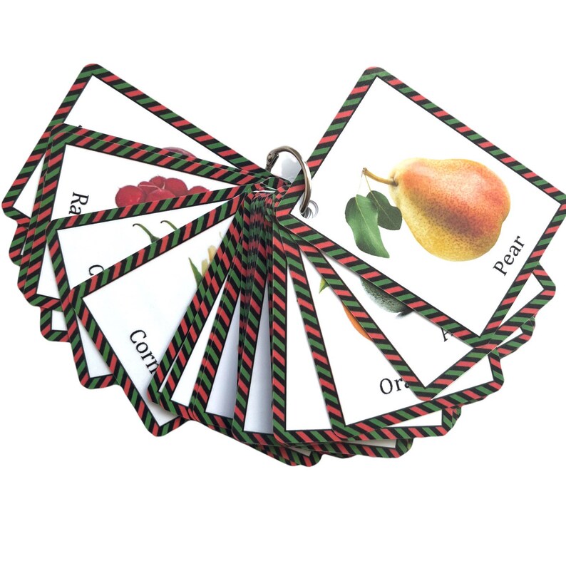 Op de afbeelding: Een set ge&iuml;llustreerde flashcards met verschillende soorten fruit en groenten, samengebonden met een metalen ring. Elke kaart heeft een witte achtergrond met een kleurrijke afbeelding en de naam van het product. De kaarten zijn omrand met een rood, groen en zwart gestreept patroon.
