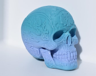 May include: A blue and purple skull with intricate designs and a gradient effect. The skull is made of ceramic and has a smooth finish.